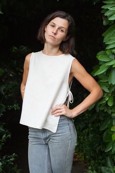 a woman is standing in front of some bushes and trees with her hands on her hips