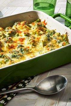 a green casserole dish with broccoli and cheese on it next to two spoons