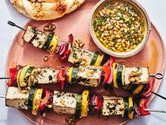 several skewers of food on a pink plate next to some pita bread