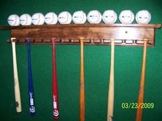 a rack with baseball bats and balls hanging on it's side, in front of a green wall