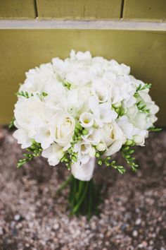 a bouquet of white flowers sitting on top of a gravel covered ground next to a wall