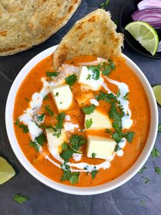 a white bowl filled with soup next to some pita bread and lime wedges