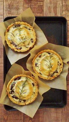 three small pies sitting on top of a black tray with wax paper around them