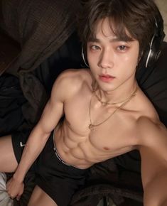 a shirtless young man laying on top of a bed with headphones around his neck