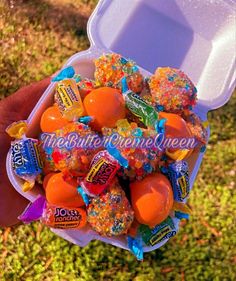 a person holding up a plastic container filled with oranges and candies on top of green grass