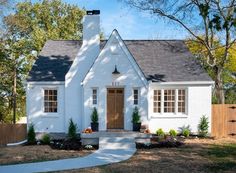 a small white house with a brown door and windows in the front yard is surrounded by trees