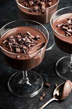 three glasses filled with chocolate desserts on top of a black counter next to a spoon