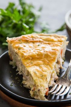 a slice of quiche on a black plate with a fork and parsley in the background