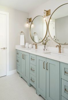 a bathroom with two round mirrors above the sinks and blue cabinetry, along with white towels