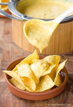 tortilla chips being dipped with cheese sauce in a bowl on a wooden table