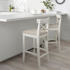 two white stools in front of a counter with a clock on the wall above it