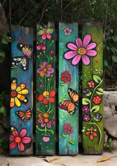 colorful painted wooden planks with flowers and butterflies on them, sitting in front of a stone wall