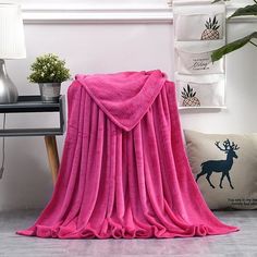 a pink blanket sitting on top of a wooden floor next to a table and lamp