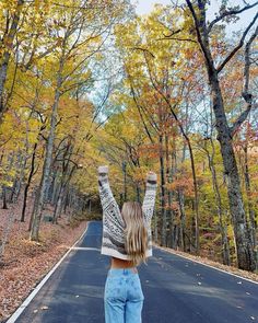 a woman standing on the side of a road with her arms in the air