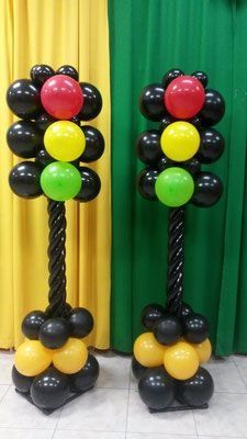 two black, yellow and red balloons are standing next to each other in front of a green curtain