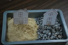 two houses made out of sand and gravel in a blue tray on a wooden table