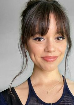 a close up of a person wearing a tank top and smiling at the camera with her hair in a bun