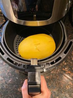 a person holding a yellow object in front of an automatic coffee maker on a counter