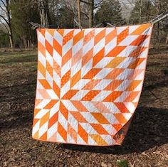 an orange and white quilt hanging on a clothesline in the woods with trees behind it