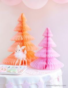 a table topped with pink and orange paper christmas trees next to a tray filled with cake