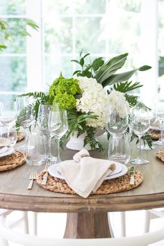 a wooden table topped with lots of white flowers and greenery next to wine glasses