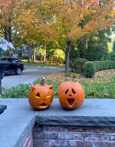 two pumpkins with faces carved into them sitting on the side of a brick wall