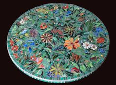 a round glass table with flowers and leaves on it's surface, against a black background