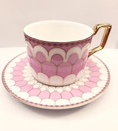 a pink and white coffee cup on a saucer with a gold handle sitting on a plate