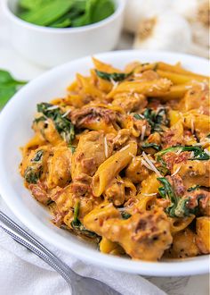 a white bowl filled with pasta and spinach on top of a table next to silverware