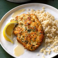 a white plate topped with chicken and rice next to a lemon wedge on top of a green table