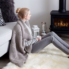 a woman sitting on the floor in front of a fire place holding a coffee cup