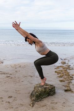 a woman doing yoga on the beach with her hands in the air while standing on top of a rock