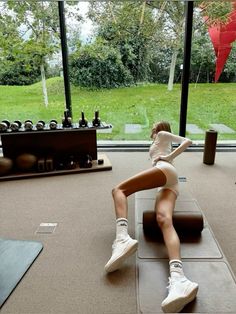 a woman sitting on top of a mat in front of a window with yoga mats