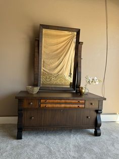 an old dresser with a mirror and vase on it in front of a beige wall