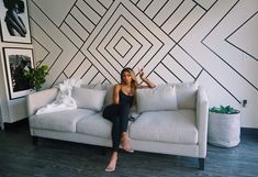 a woman sitting on top of a white couch in front of a black and white wall