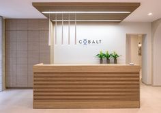 an office lobby with a wooden reception desk and planters on the counter, in front of a sign that reads cobaltt