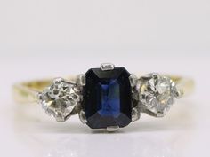 "This stunning ring holds an unusual emerald cut Sapphire, deep blue in colour flanked by two transitional cut sparkling Diamonds. The Sapphire weighs an approximate one carat and measures 4mm x 6mm and is in a six prong setting. Flanked by transitional cut Diamonds each weighing 0.25 carats a total of 0.50 carats. Quality:  H Colour  Clarity:  VS1 The ring dates Circa 1930's The Diamonds cut during this period, from about the 1920s through the 1940s, are often referred to in the trade as \"tran Blue Radiant Cut Three-stone Ring, Classic Blue Radiant Cut Emerald Ring, Emerald Cut Three Stone Sapphire Ring, Blue Rectangular Sapphire Ring With Brilliant Cut, Blue Emerald Cut Three Stone Ring, Three Stone Emerald Cut Sapphire Ring, Gold Engagement Dress, Trilogy Ring, Engagement Dress