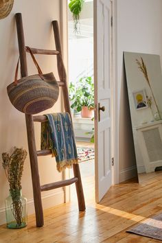 a ladder leaning against the wall with a basket on it's back, next to a potted plant