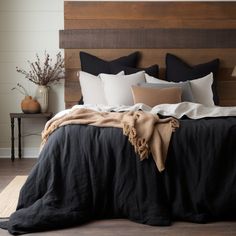 a bed with black linens and pillows on top of it, along with a wooden headboard