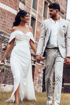 a man and woman holding hands walking in front of an old brick building with tall windows