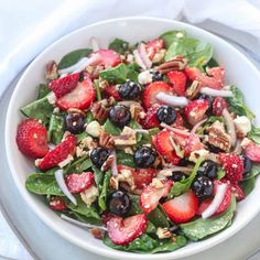 a white bowl filled with spinach, strawberries and nuts on top of a table