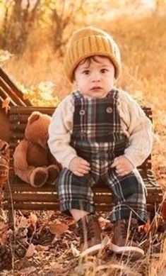 a little boy sitting on top of a bench with a teddy bear next to him