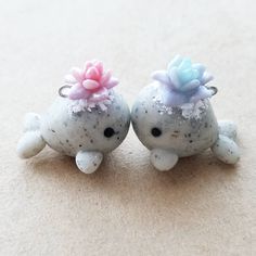 two little sea animals with flowers on their heads sitting next to each other in the sand