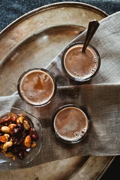 three glasses filled with drinks sitting on top of a metal tray next to a spoon