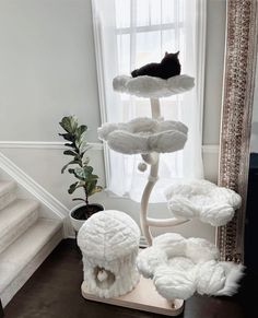 a cat sitting on top of a tree in the middle of a room with stairs