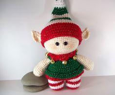 a crocheted christmas elf doll sitting next to a rock on a white surface