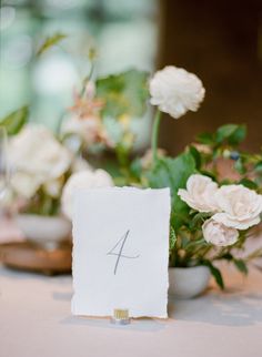 the table numbers are displayed on napkins with flowers in vases behind them, along with wine glasses