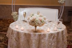 a table topped with a vase filled with flowers next to two wine glasses and candles