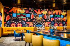 a brightly colored restaurant with yellow chairs and blue counter tops, decorated with colorful floral wallpaper