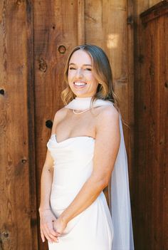 a woman in a white wedding dress standing next to a wooden wall wearing a veil